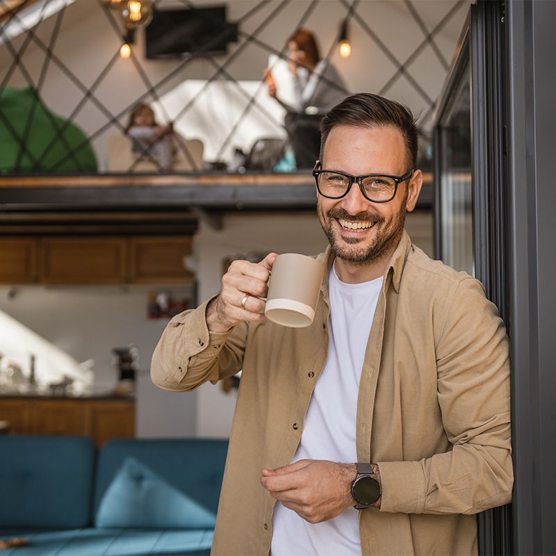 A man smiling warmly, holding a coffee mug at home
